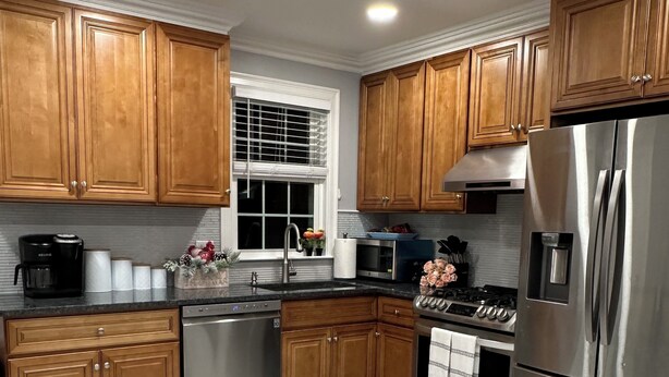 A modern kitchen with wooden cabinets, stainless steel appliances, a built-in oven, and a window with blinds. - North End Retreat (Manchester)