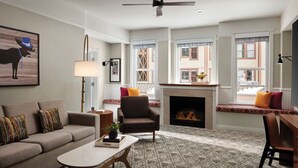 A living room with a sofa, armchair, coffee table, fireplace, and large windows with a view of buildings.