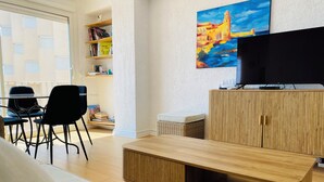 A modern living room with a wooden coffee table, a white sofa, a black chair, a bookshelf, a flat-screen TV, and a painting on the wall. - 🌷 Superb apartment - magnificent view of the Port 🌷 (Saint-Cyprien)