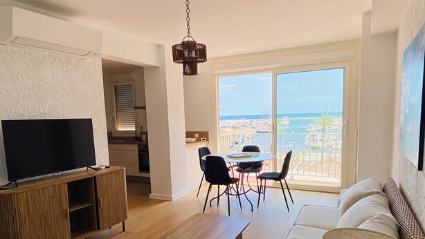 A modern living room with a wooden coffee table, a TV on a wooden cabinet, a wicker sofa, and a dining area with chairs and a table. - 🌷 Superb apartment - magnificent view of the Port 🌷 (Saint-Cyprien)