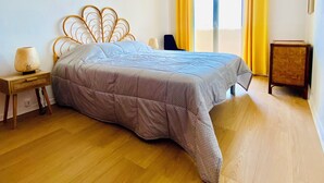A bedroom with a bed, a bedside table, a lamp, a chair, a small table, a wall-mounted air conditioner, and a window with curtains. - 🌷 Superb apartment - magnificent view of the Port 🌷 (Saint-Cyprien)