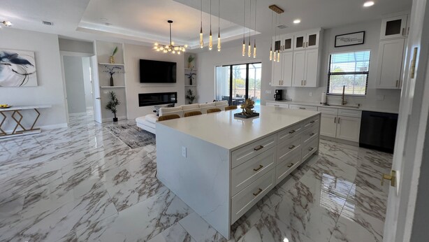 Una cocina moderna con una isla grande, armarios blancos y piso de mármol.