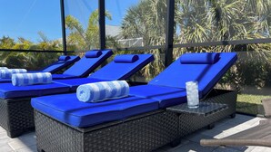 Sillones de exterior con cojines azules y toallas enrolladas, dispuestos en un patio con vistas a palmeras.