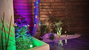 A landscaped outdoor area with a wooden fence, a tree wrapped with colorful lights, and various plants in planters. - NEW 2 Bed2 Bath Tropical Villa.Ultimate Escape! Private Pool.Covered Patio & BBQ (Savaneta)