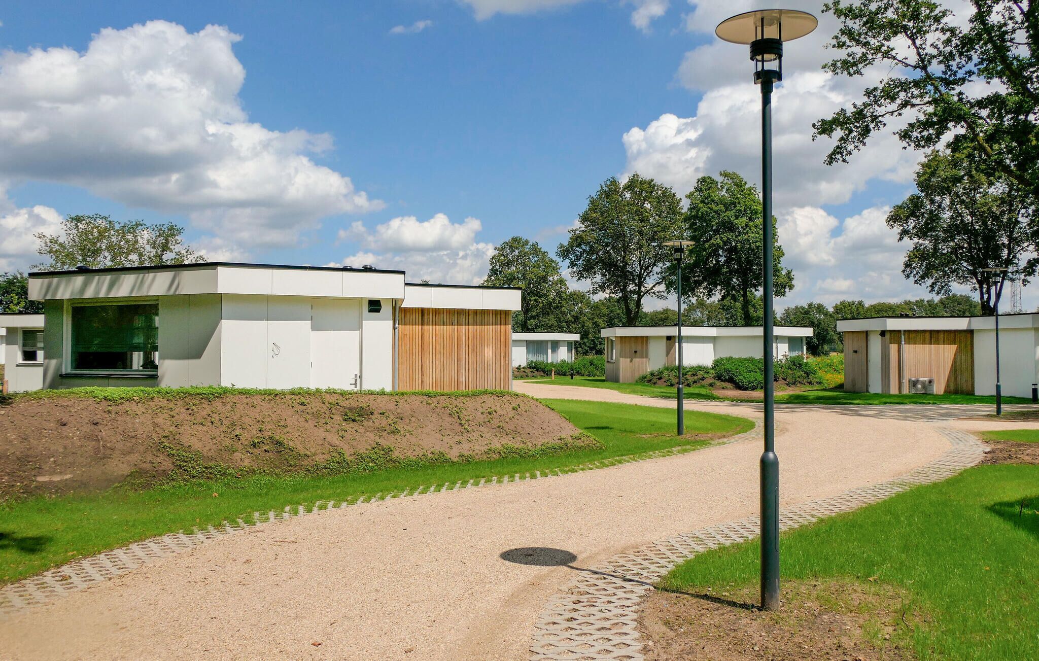 Un espace extérieur moderne avec un chemin menant à plusieurs petits bâtiments de plain-pied, dotés de grandes fenêtres et d’éléments décoratifs en bois.