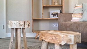 Una habitación con una mesa de centro de madera y dos taburetes, una estantería y un sofá con cojines a rayas.