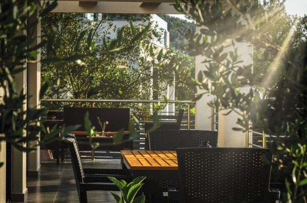 An outdoor seating area with tables and chairs, surrounded by greenery and a view of trees and a building.