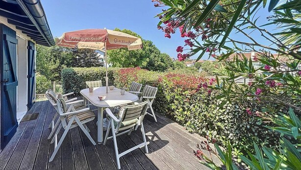 An outdoor patio with a table and chairs, a red umbrella, and lush greenery. - Maison 5 Cantons Anglet (ANGLET)