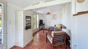 A spacious living area with a white cabinet, a sofa, a wooden chair, and a TV. - Maison 5 Cantons Anglet (ANGLET)