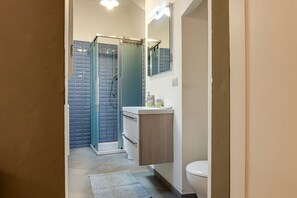 A bathroom with a glass shower enclosure, a white toilet, and a wooden vanity with a mirror.