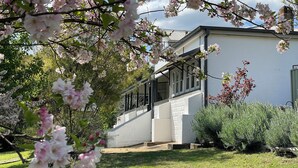 A building with a white exterior, a staircase leading to the entrance, and a garden with blooming flowers.