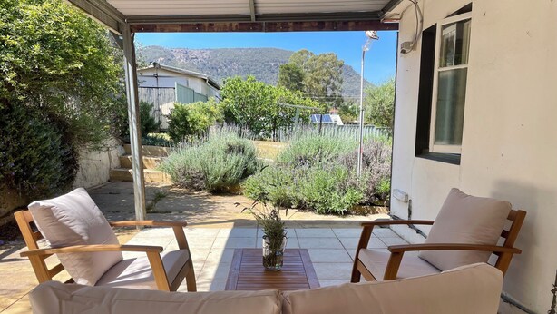 A covered patio with wooden furniture and a view of a garden and mountains.