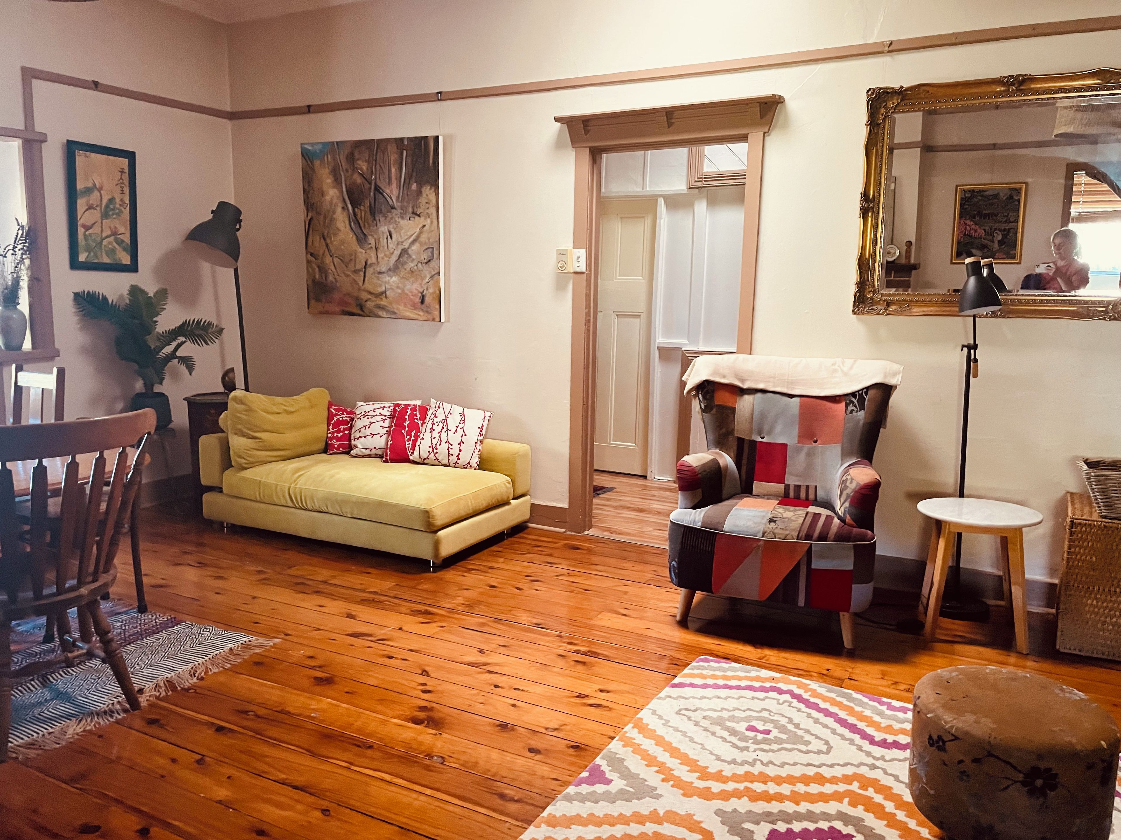 A living room with a yellow sofa, a patterned armchair, wooden flooring, and a large mirror.