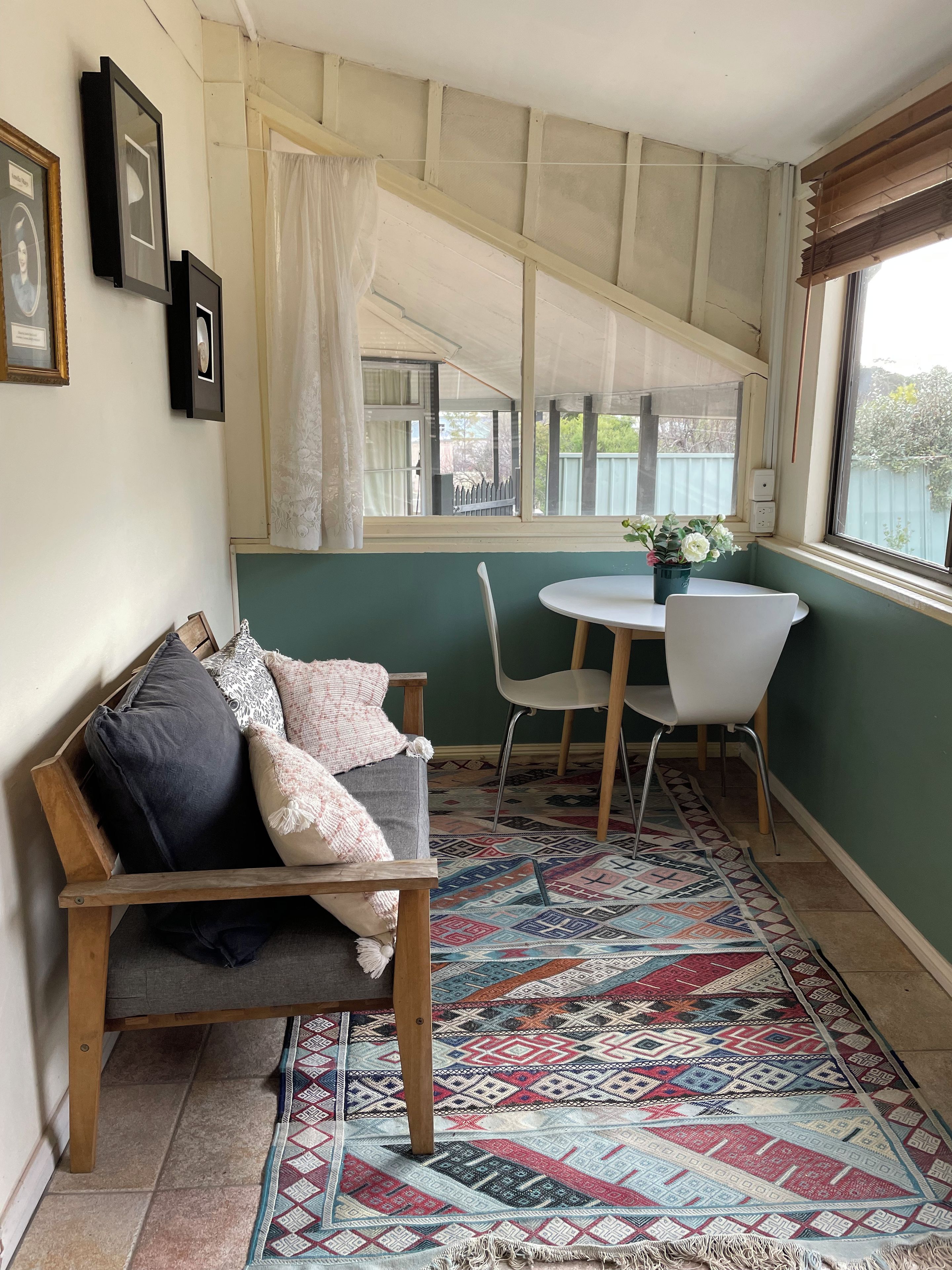 Une pièce chaleureuse avec un banc en bois, une table blanche avec des chaises, un tapis à motifs et des tableaux encadrés accrochés au mur.