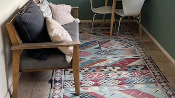Une pièce chaleureuse avec un banc en bois, une table blanche avec des chaises, un tapis à motifs et des tableaux encadrés accrochés au mur.