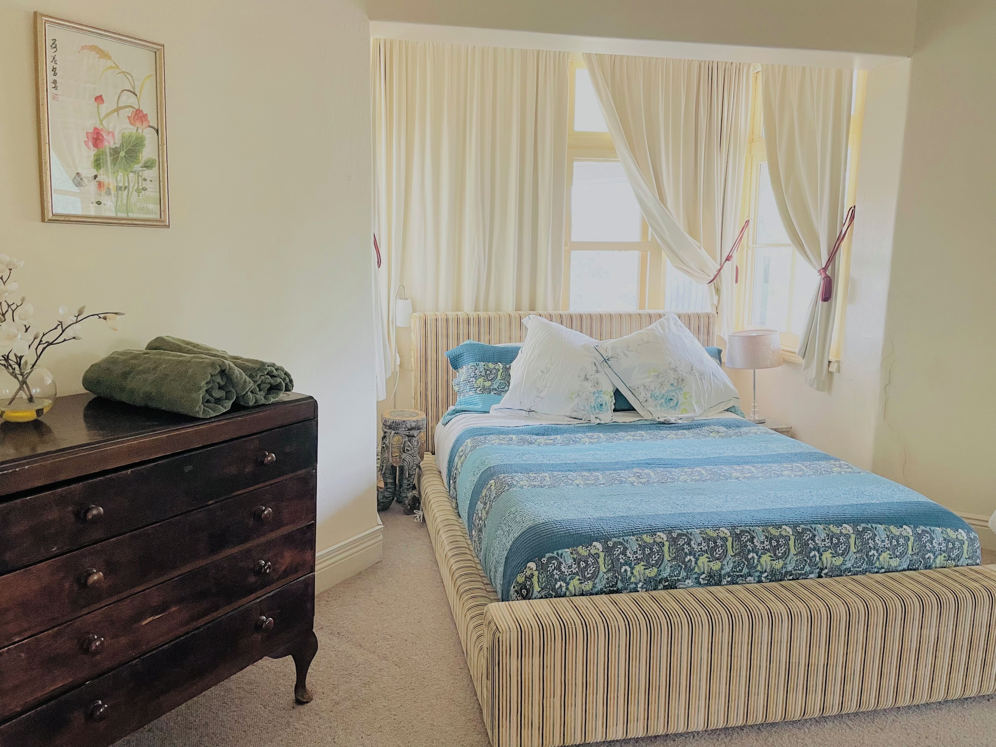 A bedroom with a bed, a dresser, a nightstand, and a window with curtains.
