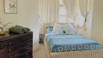 A bedroom with a bed, a dresser, a nightstand, and a window with curtains.