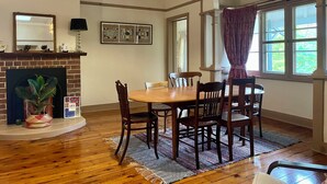 A dining area with a wooden table and chairs, a fireplace, a chandelier, and a window with curtains.