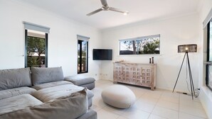 A modern living room with a grey sofa set, a wooden cabinet, a floor lamp, and a TV on the wall.