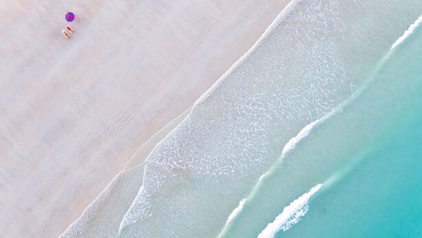 An aerial view of a beach with a clear demarcation between the sand and the turquoise water.