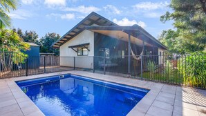 A modern house with a swimming pool, a covered patio, and a fenced backyard.