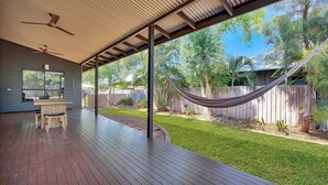 A covered patio with a wooden deck, a dining table with chairs, and a hammock.