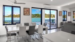 Een moderne eetruimte met uitzicht op zee, een plafondventilator en een balkon met een hekwerk.