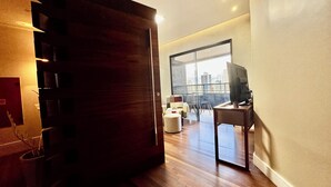 A modern living room with a wooden floor, a large window, and a television. - COP 30 TWO SUITES (Umarizal Belém)