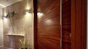 A hallway with wooden flooring, a potted plant, a shelf with a light, and a wooden door. - COP 30 TWO SUITES (Umarizal Belém)