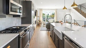 A modern kitchen with dark cabinetry, stainless steel appliances, and a large island with a sink. - Bright/Beautiful new townhome near Old Town Arvada/Quick access to the Mountains (Arvada)