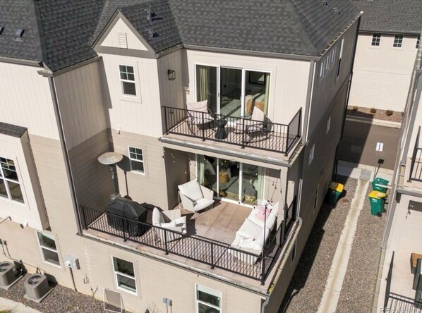 Een woongebouw met twee verdiepingen, een balkon op de bovenste etage, buitenmeubilair en een zichtbare afvalbak.