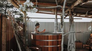 A rustic outdoor sauna with a wooden barrel design, surrounded by a wooden fence and a corrugated metal wall. - Shepherd's Story, Ross (Ross)