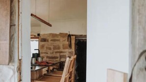 A rustic kitchen with a wooden table and chairs, a stone wall, and a hanging pot rack. - Shepherd's Story, Ross (Ross)