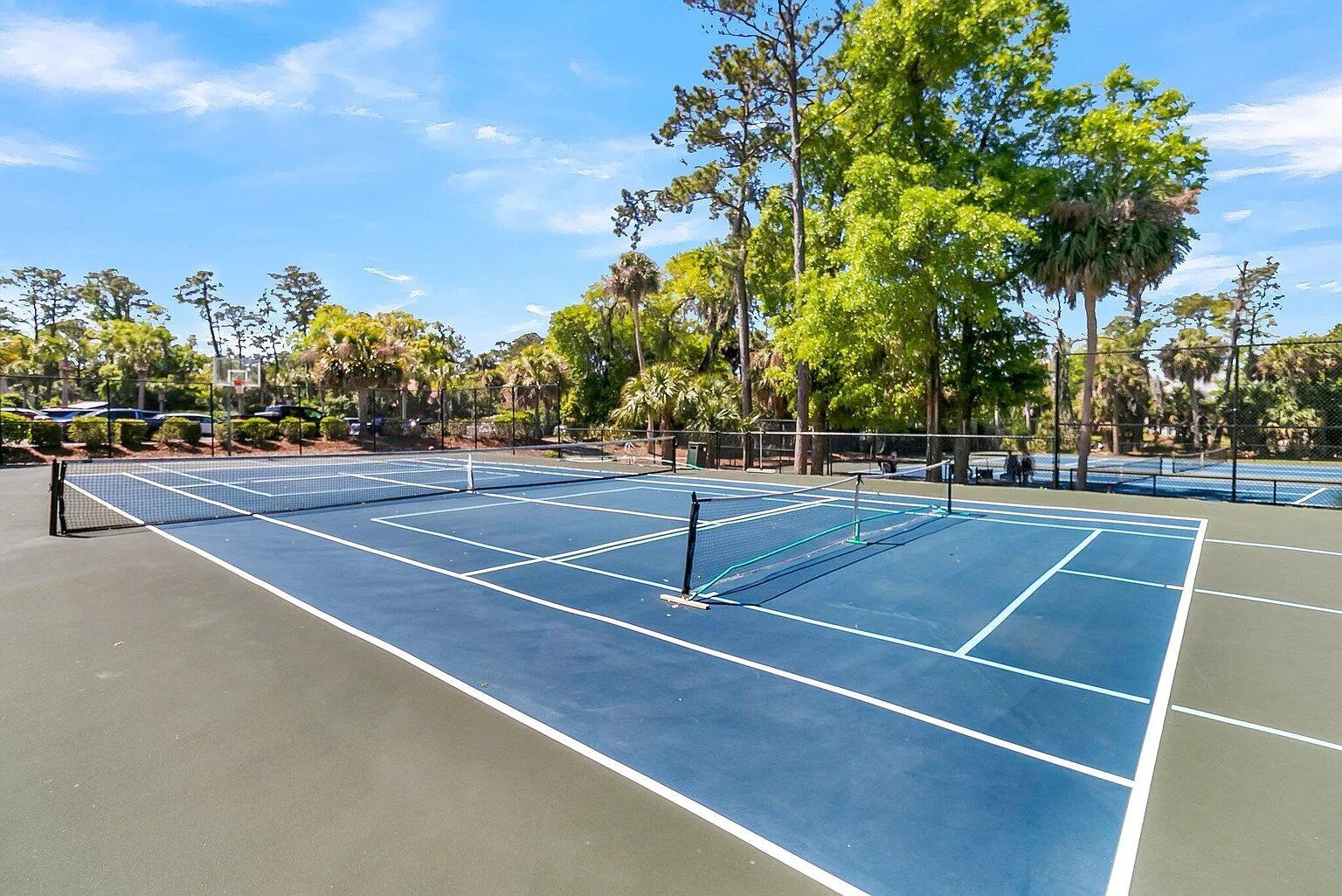 Una cancha de tenis con red, rodeada de árboles y un cielo despejado.