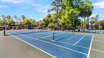 Una cancha de tenis con red, rodeada de árboles y un cielo despejado.