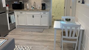 Una cocina moderna con armarios blancos, un horno empotrado y un microondas. Hay una zona de comedor con una mesa y sillas, y una alfombra estampada en el suelo.