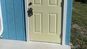 Una puerta verde claro con un letrero que dice 'Se busca personal para lavandería' en un edificio con revestimiento azul.