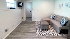 Un salón con un sofá gris, alfombra estampada y un televisor en la pared.