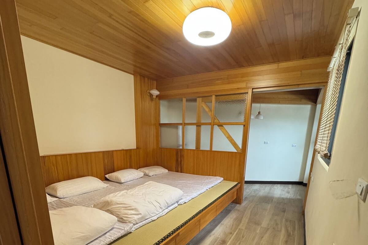 A room with a wooden bunk bed, a ceiling light, and a window with a view.