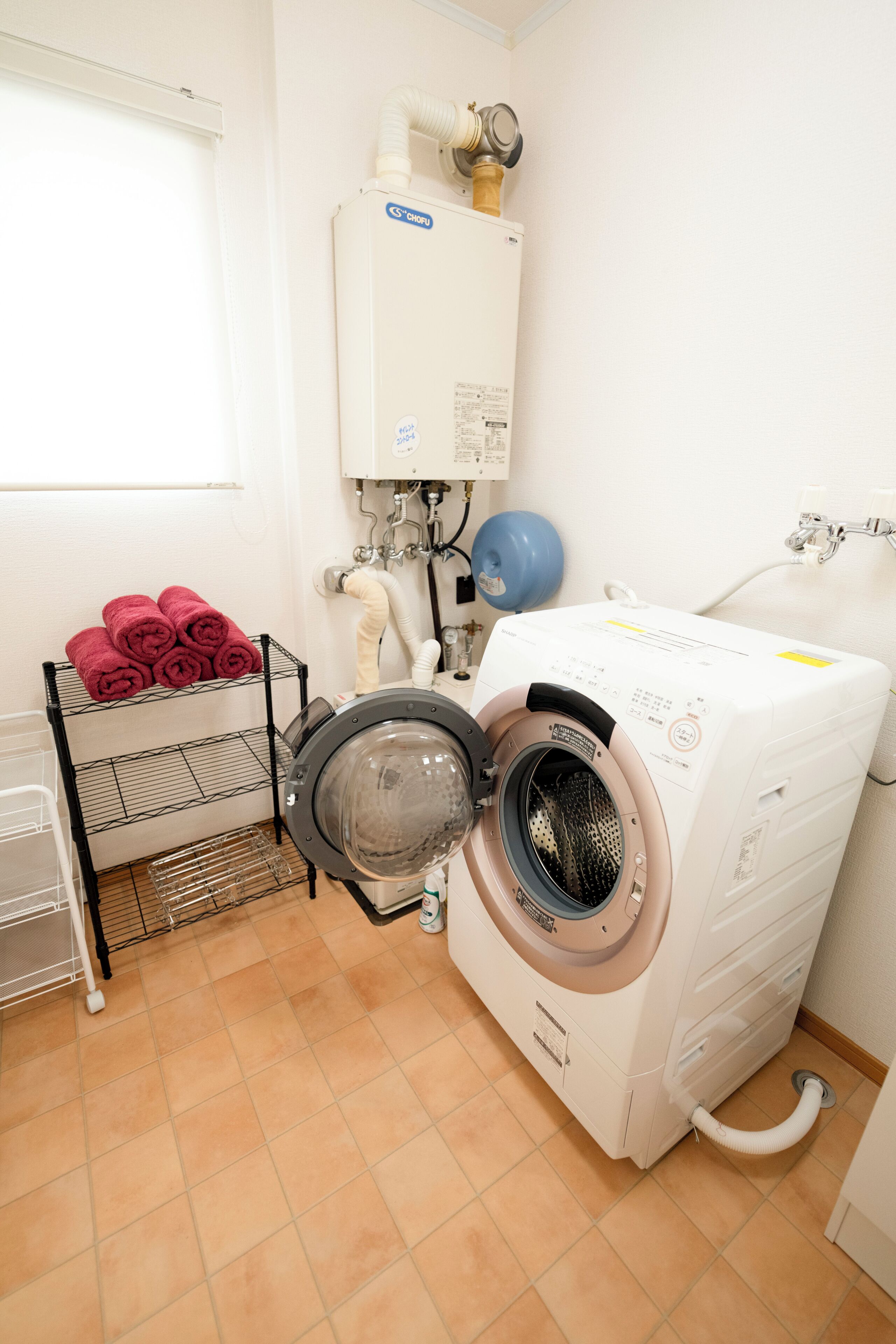 A laundry room with a front-loading washing machine, a drying machine, and a rack with folded towels.