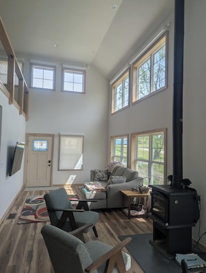 A spacious living room with a fireplace, large windows, a cozy seating area, and a TV mounted on the wall.