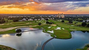 Un parcours de golf avec un grand étang, un pont et un bâtiment en arrière-plan.