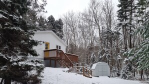 Una casa con terraza de madera y garaje, rodeada de árboles cubiertos de nieve.
