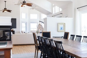 A spacious dining area with a long wooden table and black chairs, a fireplace with a modern design, and a hanging chair. - Sea Forevermore: Oceanside, Private Pool, 2 Hot Tubs, Elevator (Corolla)