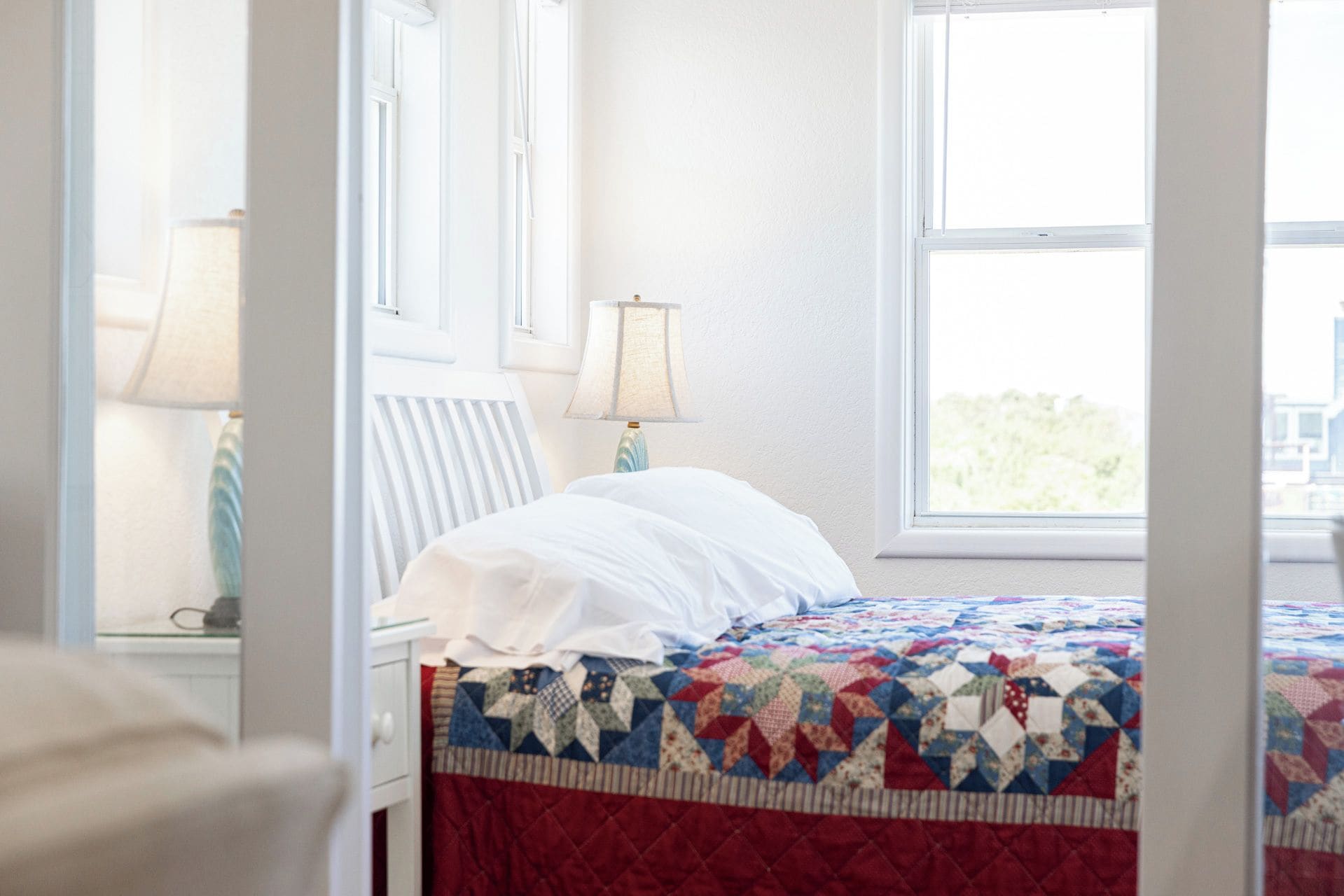 A bed with a quilt, a nightstand with a lamp, and a window with a view.