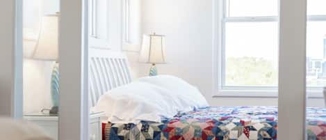 A bed with a quilt, a nightstand with a lamp, and a window with a view.