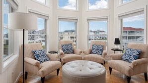 Una habitación amplia con ventanas grandes, cuatro sillones a rayas, un otoman redondo y una lámpara de pie.