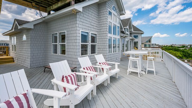 Una terraza con sillas Adirondack blancas y una mesa, con vista a una zona residencial.