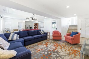 A living room with a blue sofa, a red armchair, and a patterned rug. - Sea Forevermore: Oceanside, Private Pool, 2 Hot Tubs, Elevator (Corolla)