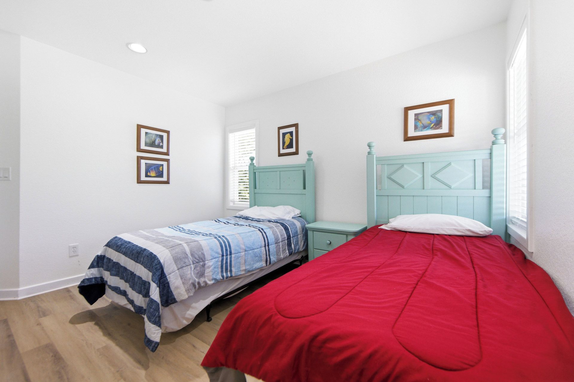 A bedroom with two beds, a window with blinds, and framed pictures on the wall.